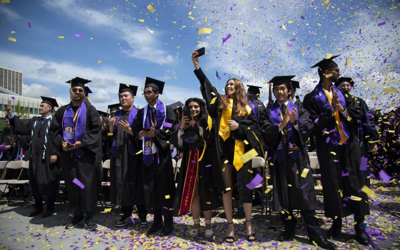 Purple and gold confetti surrounds new graduates at the UAlbany Entry Plaza lawn.
