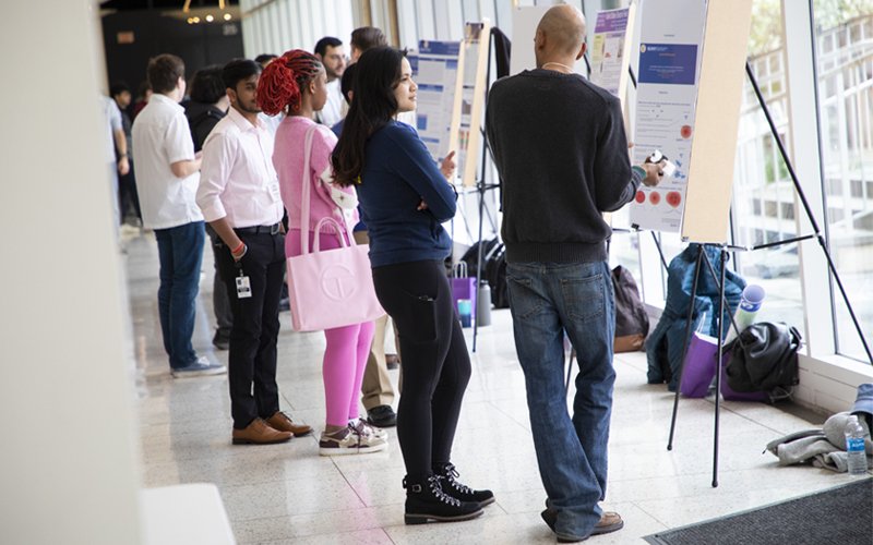 Groups of students stand in a hallway discussing various posters on display.
