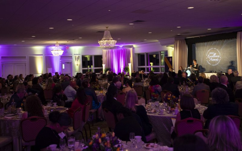 A room full of people at round tables set for dinner and adorned with purple and gold tulips
