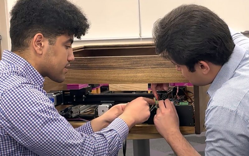two students work on a mechanical device designed to remove the cover on reams of paper.