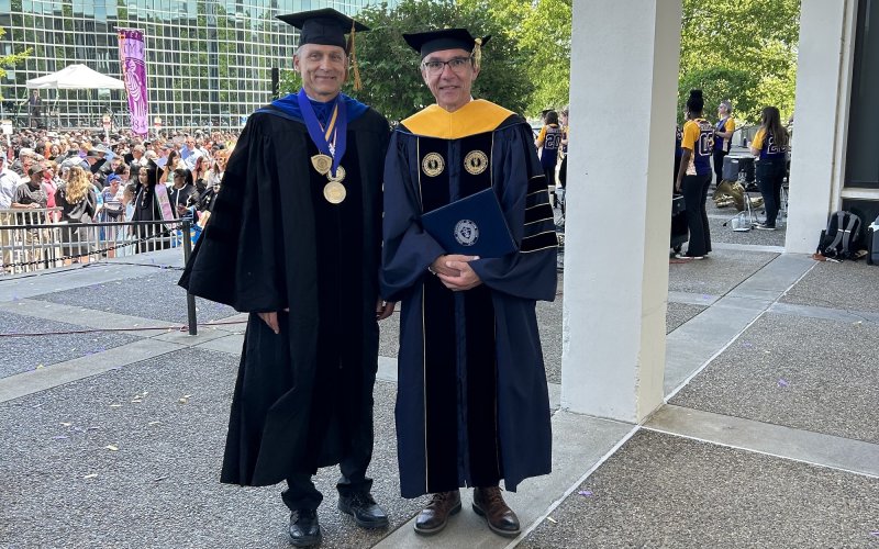 Igor Lednev and Jürgen Popp stand in academic regalia on the academic podium following UAlbany's 2023 undergraduate commencement ceremony.