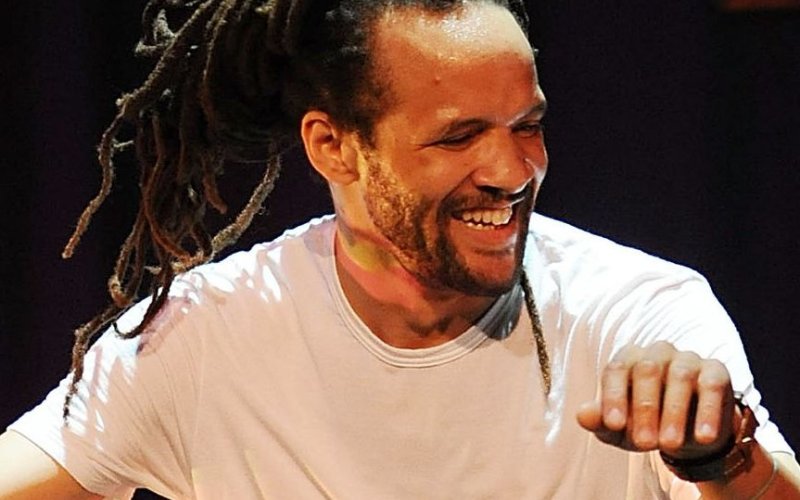 man with dreadlocks in white shirt looks over his shoulder and smiles