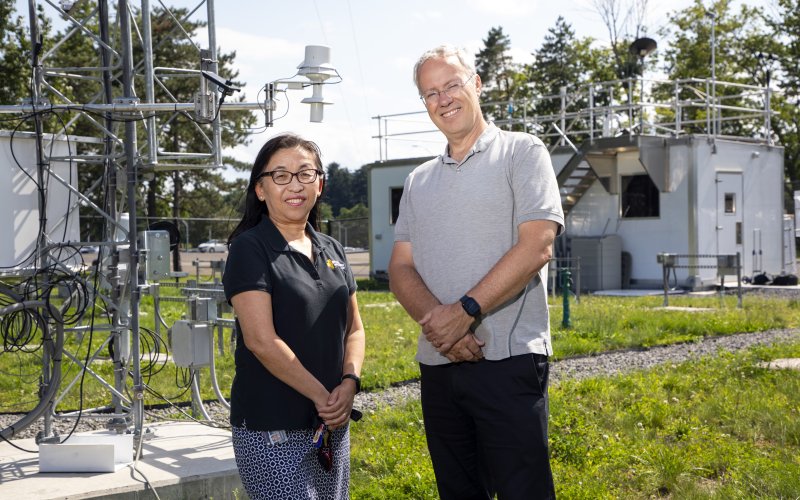 NYS Mesonet Program Manager June Wang (left) and Director Chris Thorncroft stand in front of a Mesonet weather tower at the ETEC research and development complex on UAlbany’s campus.