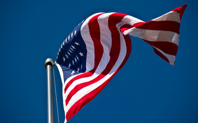 The American Flag waves in the wind against a bright blue sky.