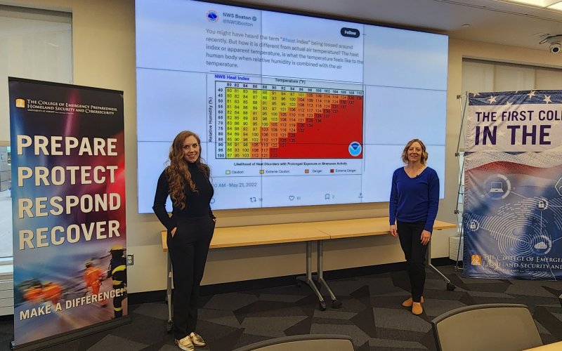 Micki Olson and Jeannette Sutton stand in front of a screen displaying a National Weather Service tweet at the CEHC Ops Command Center.