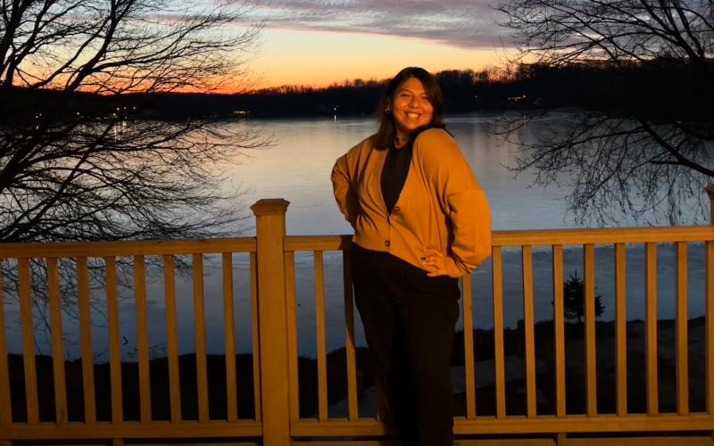 Sapphire Correa stands in front of a lake. The sun is setting behind the lake.
