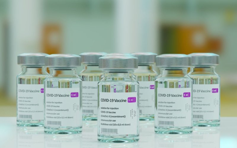 Seven bottles of the covid-19 vaccine are on a smooth white tabletop with blurred background.