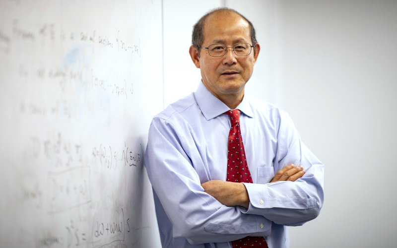 Professor of Mathematics Kehe Zhu stands next to an equation on a whiteboard.
