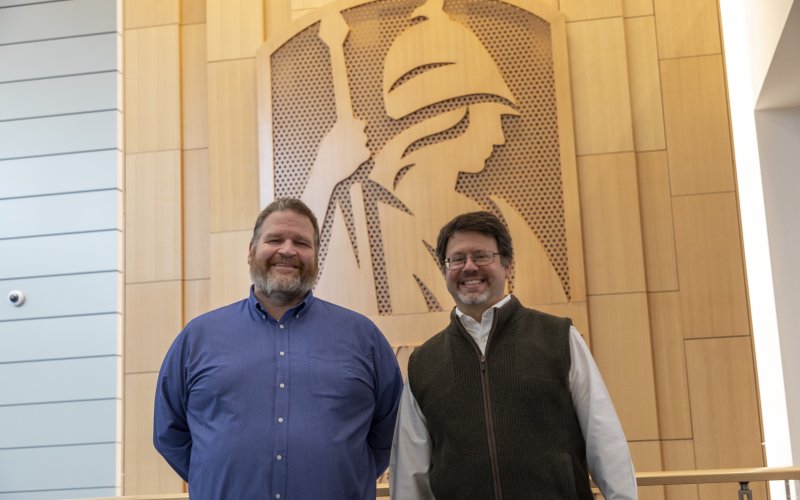 CEHC's Brandon Behlendorf and Interim Director of the Institute for Artificial Intelligence Eric Stern stand in front of the Minerva wall in the ETEC atrium.