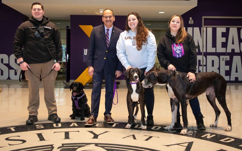 Two men, two women and three dogs line up in the University Hall atrium for a photo.