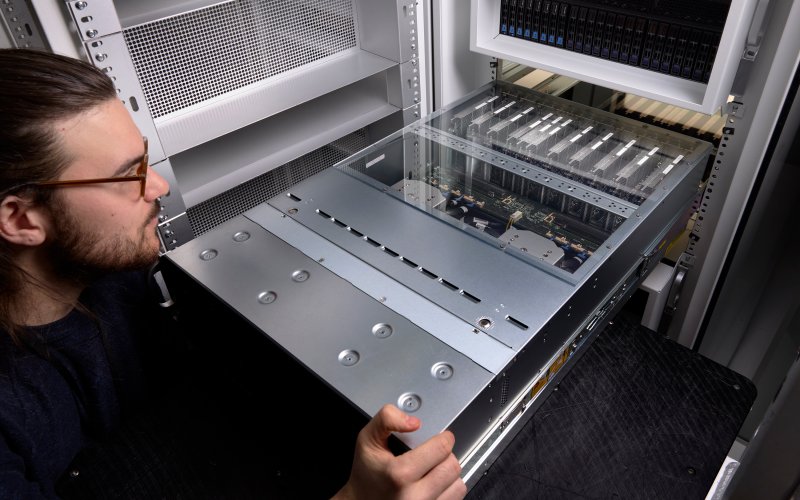 A person in the foreground slides a metallic silver computer node into a server rack.