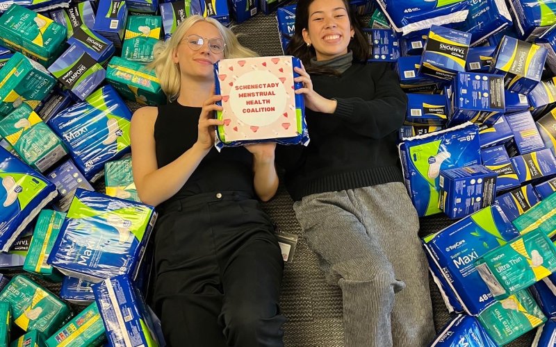 Brynn and Claire lay on their backs and are surrounded by period products.