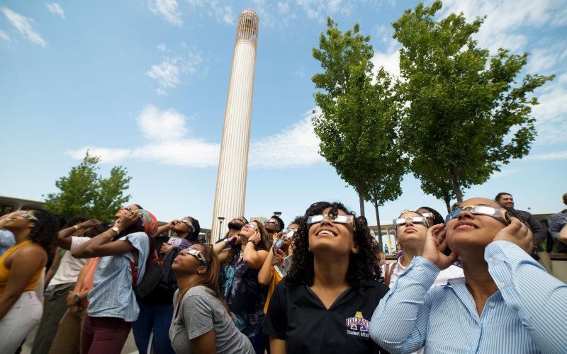 A crowd of people wearing eclipse glasses looks up at the sky under the UAlbany Carillon ahead of the 2017 solar eclipse.