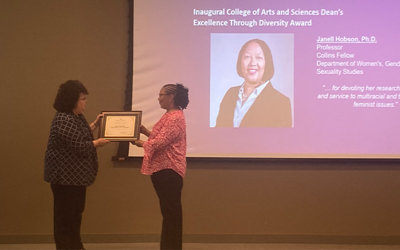 Janell Hobson stands on stage and accepts the inaugural College of Arts and Sciences Excellence Through Diversity Award from Dean Jeanette Altarriba