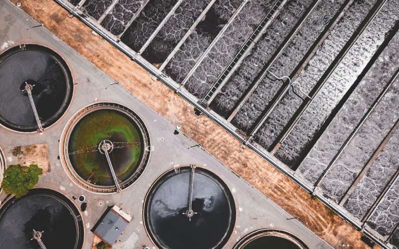 Aerial image of a wastewater treatment facility. The top right half of the image shows water being treated in a rectangular holding pool. On the bottom left, water is held in circular tanks.