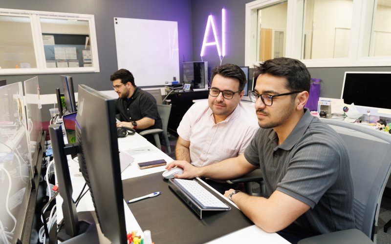 Abdullah Canbaz and Mikail Demir stare at a computer screen inside the AI in Complex Systems Lab.