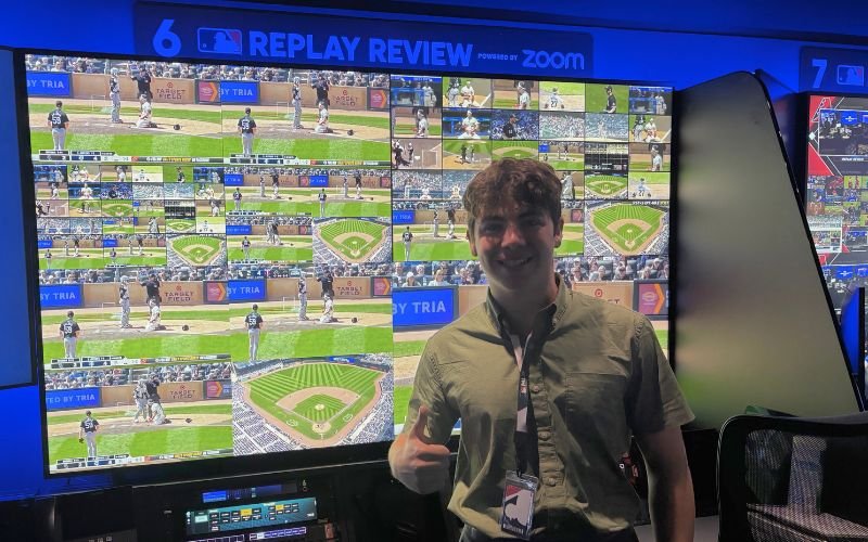 CEHC student Roberto Friedlander stands in front of monitors showing different views of the baseball field. 
