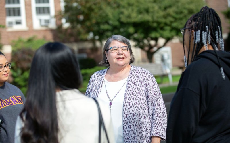 Victoria Rizzo smiles and speaks with three students outside on UAlbany’s Downtown Campus.