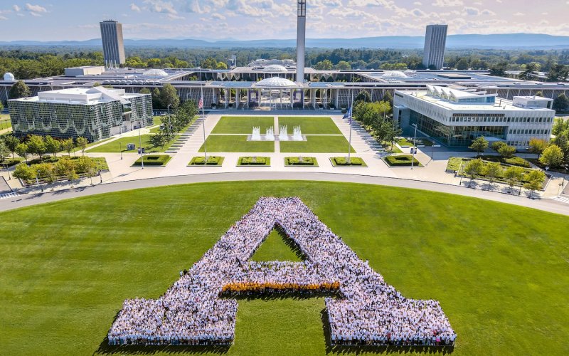 UAlbany students wearing white t-shirts form a large A on the grass in Collins Circle in front of the University at Albany's Entry Plaza. 
