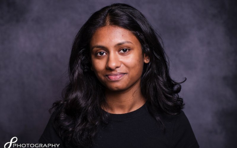 A young woman with long hair wearing a black shirt, looking confidently at the camera. 