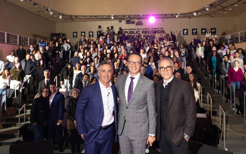 UAlbany alums Monte and Avery Lipman pose with Mike Christakas, Dean of Students, in front of a full auditorium. At the back of the room, the new name reads Monte Lipman '86 and Avery Lipman '88 Republic Records Music Hall.