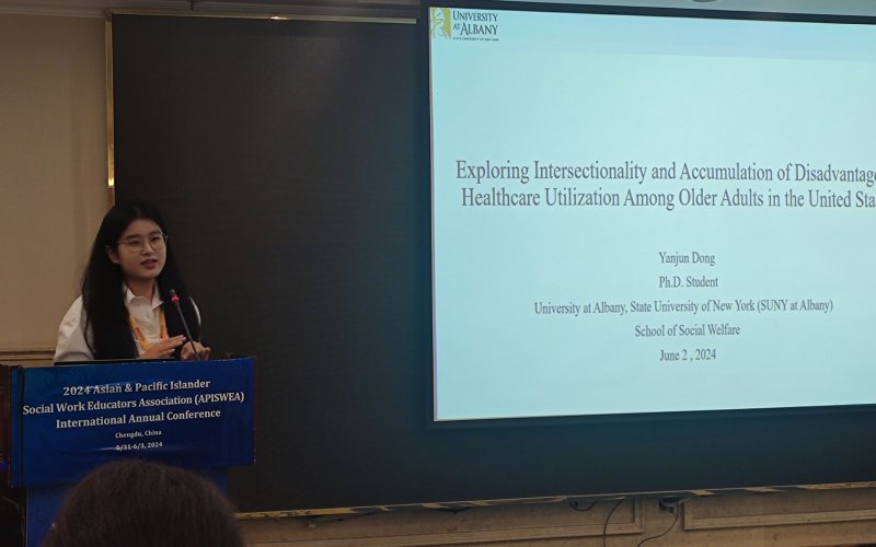 Yanjun stands behind a podium, with a slideshow behind her.