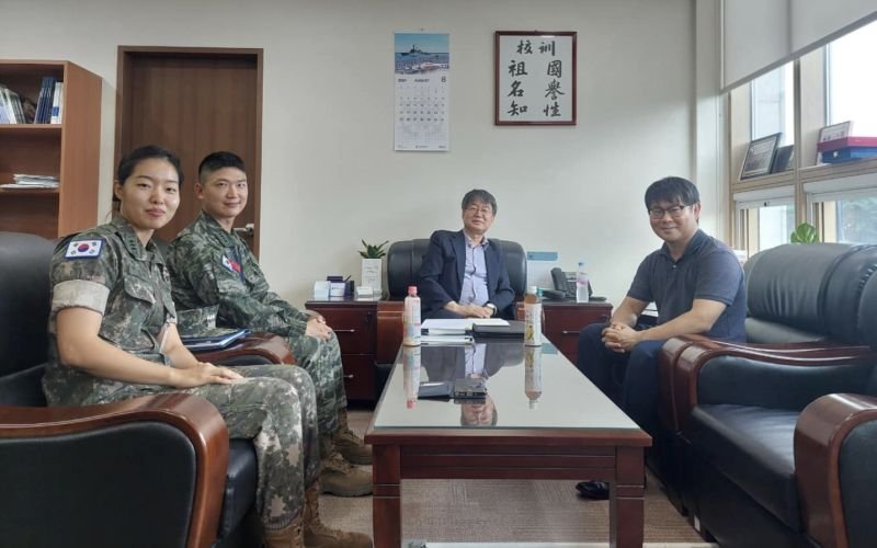 Two people in militaty fatigues and two in civilian clothing sit around a glass-topped table.