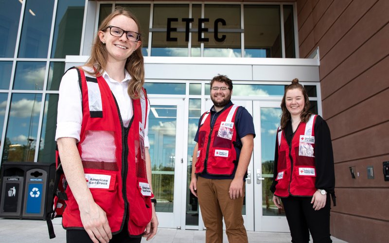 Nancy Kreis, Mike Clahane and Erin Golden stand in front of the ETEC building in American Red Cross vests.