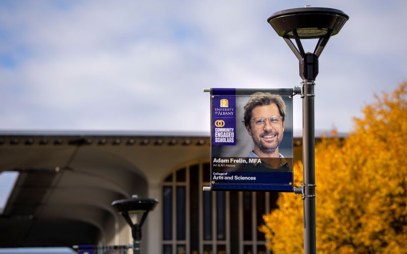 A University at Albany campus streetlight displaying a Breathing Lights banner by Associate Professor Adam Frelin.