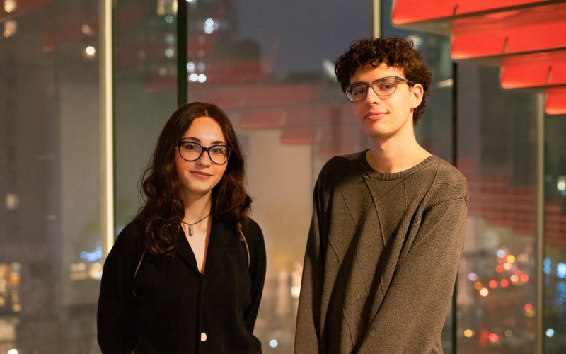two individuals in glasses look straight forward with slight smiles on their faces