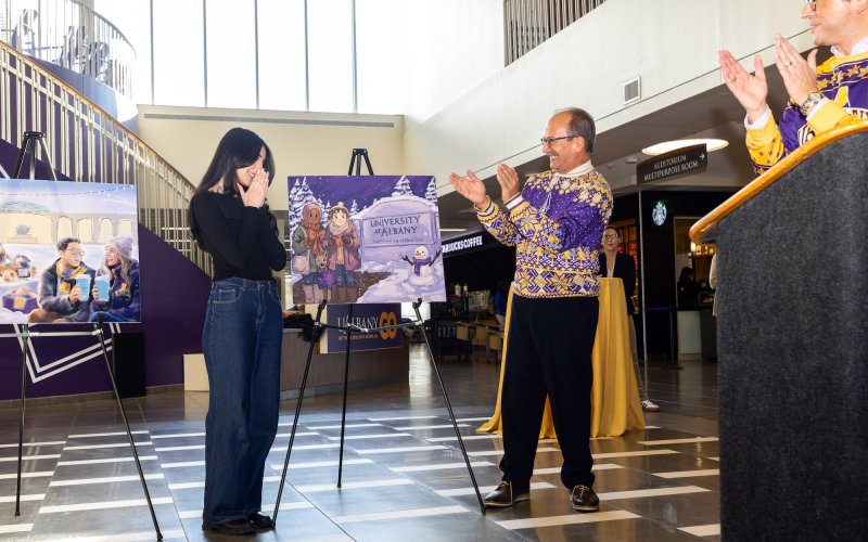 UAlbany student Sara Sadaat is applauded by President Havidan Rodriguez and VP for Student Affairs Mike Chrisakas after realizing she just won this year's annual Holiday Card Contest along with a $1500 scholarship.