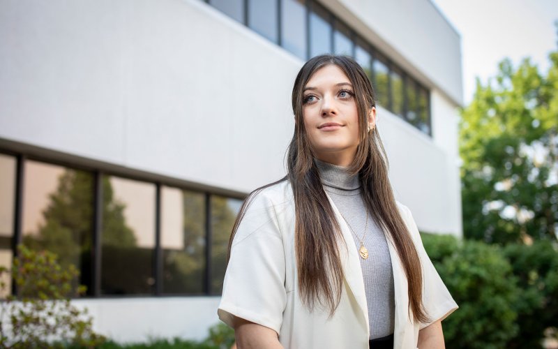 Student Cassie Kane stands in front of the School of Public Health, looking to the side.
