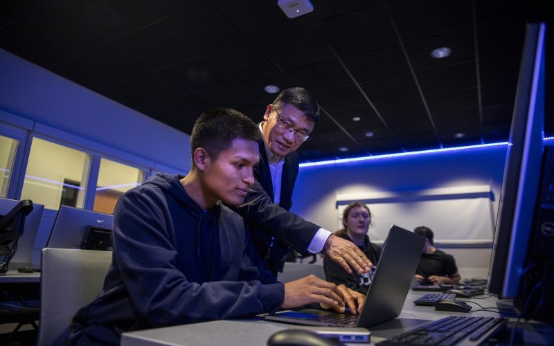 Cybersecurity professor Alan Wang works with a student on his class project from the Cyber Range lab.