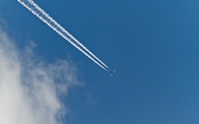 Thin white clouds form behind a jet across the sky.