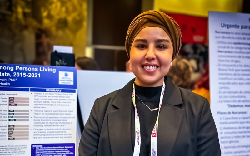 Amaal Alharbi smiles and poses for a photo in fromt of her research poster at a professional conference.