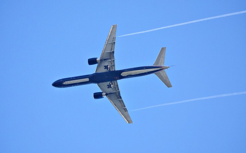 Thin white clouds form behind a Boeing 757 on a clear sky day.