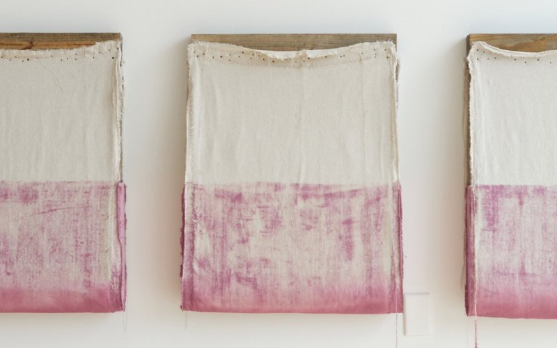 Howard Schwartzberg's work: three wooden frames with half cream and half pink cloth stapled to them hang from a wall.