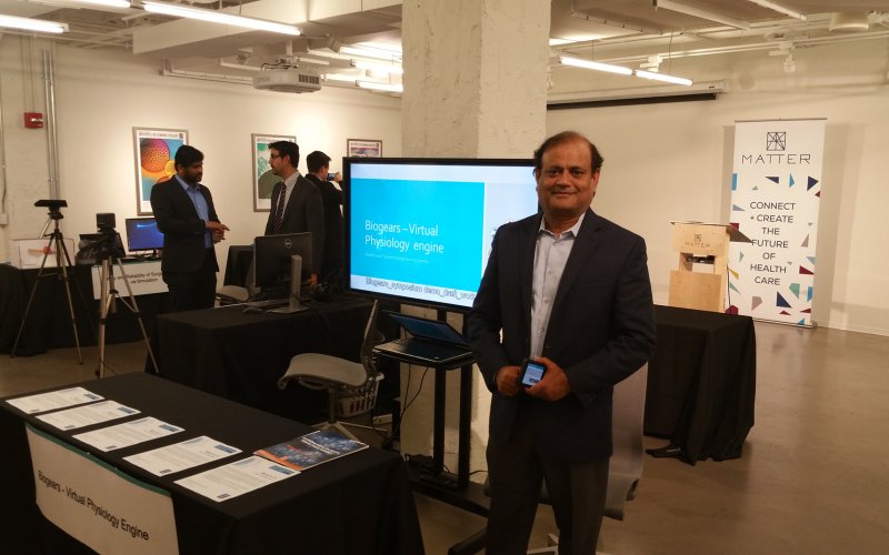Kesh Kesavadas stands in front of table and presentation screen at the MATTER conference.