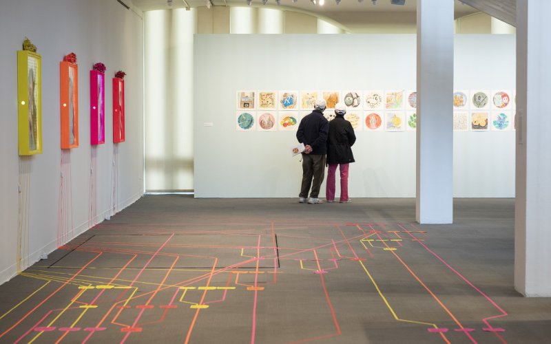 A pair of people stand in the UAlbany Museum Exhibition space, observing artwork on the wall.