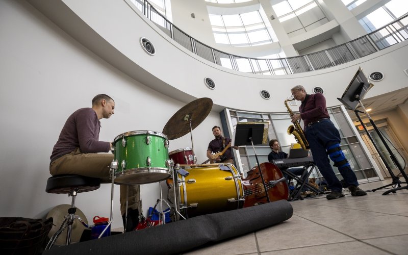 A five part jazz band plays drums, saxophone, guitar, bass and keyboards in the NanoTech complex atrium