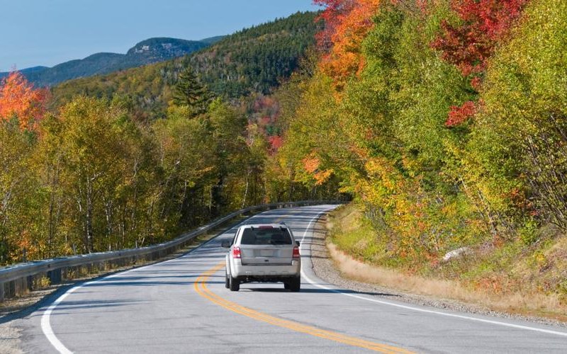 car is driving down the road surrounding by fall foliage