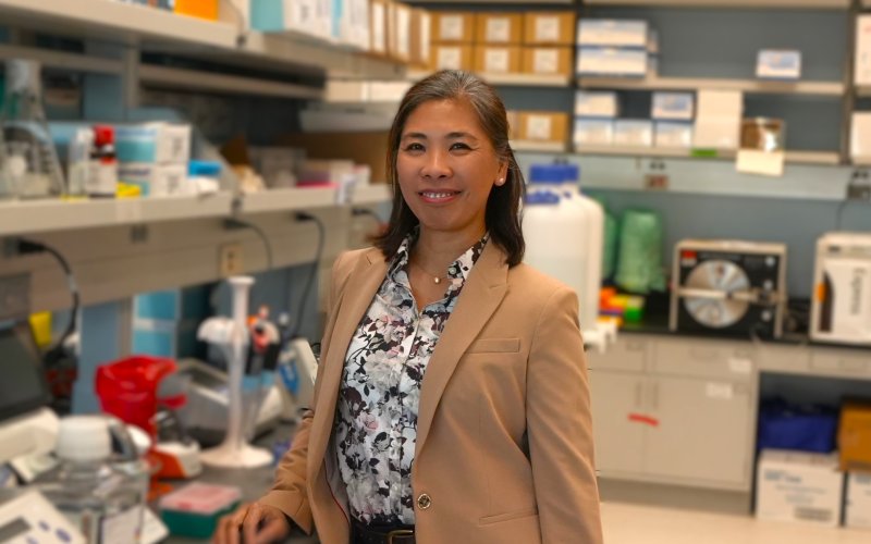 A woman in a beige blazer and floral blouse smiles, posing for a portrait, in a biology lab. 