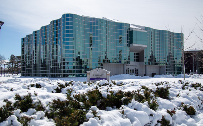 University Hall on a snowy day. The large building's glass windows gleam in the sunlight, reflecting the snowy landscape.