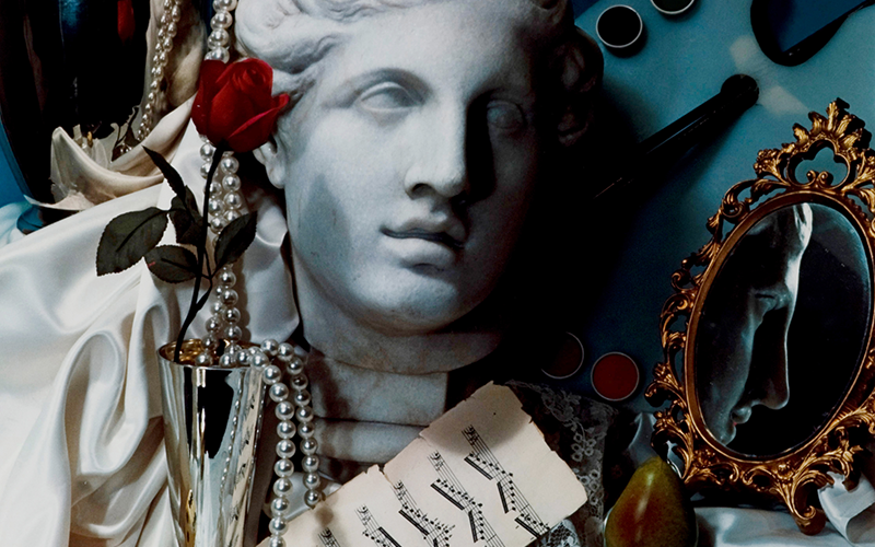 An assortment of items, a sculpted head, pearls, a vase, a rose and a mirror.