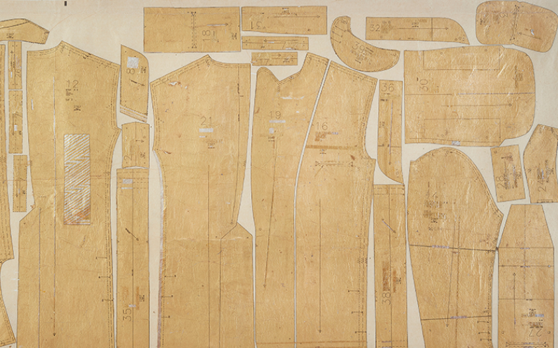 A paper sewing pattern, old and yellowed, is laid out on a panel.
