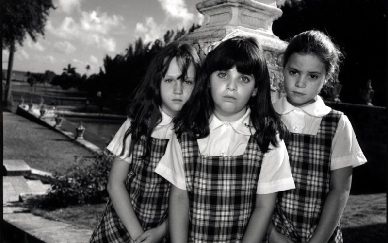 A black and white photo of three children standing in front of an old stone lantern. They are all wearing matching plaid dresses.