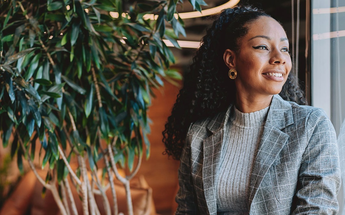 A smiling professional in communications or marketing sitting by a window holding a laptop.