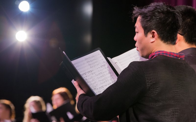 Singers stand on stage with sheet music in folders