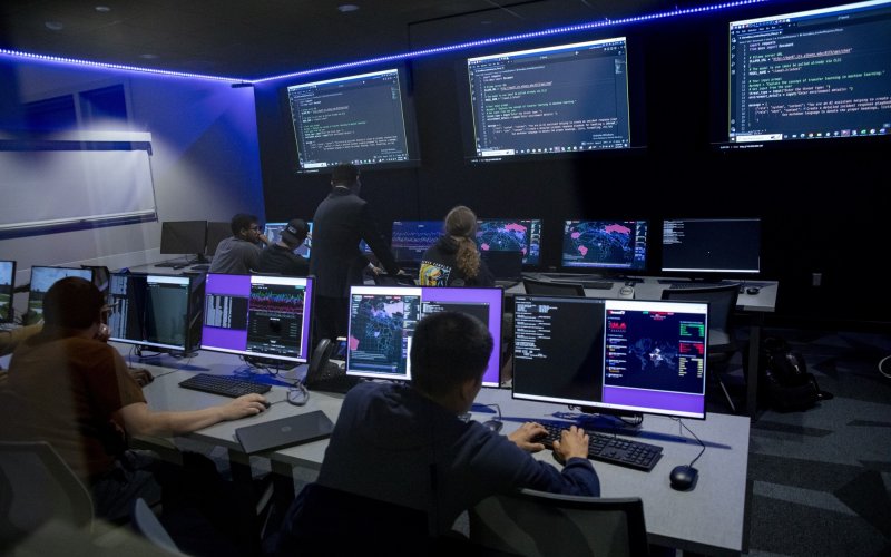 Students review code on a row of computers inside a dark lit room at ETEC.