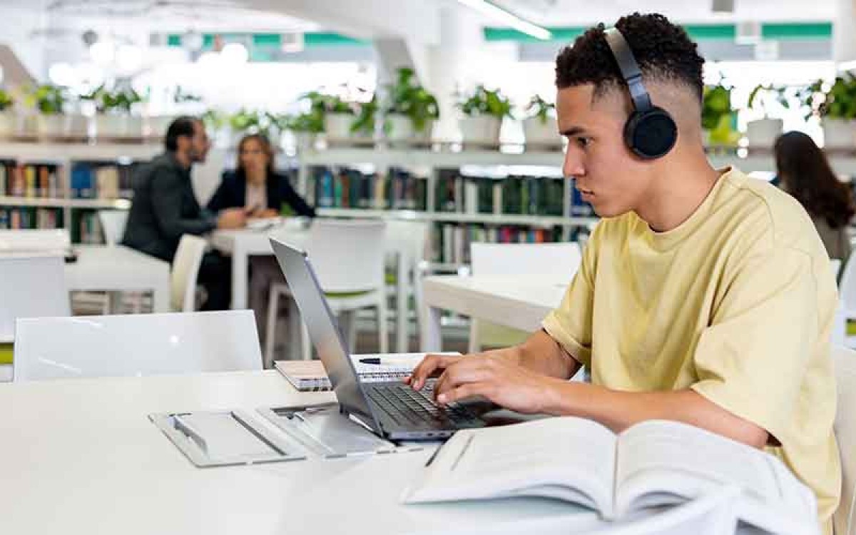 A student on his laptop in the library attends online classes.